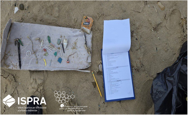 Rifiuti marini raccolti su una spiaggia, accanto a una scheda di registrazione per la loro identificazione e classificazione.